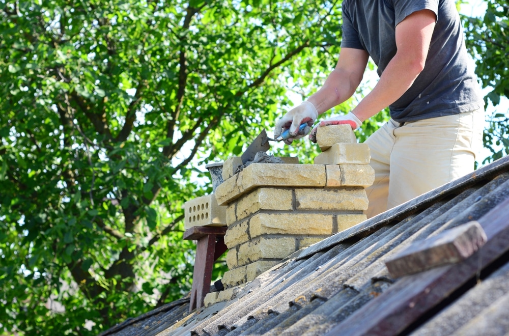 When Is Chimney Rebuilding Necessary? Warning Signs to Watch For 1 Repairing and rebuilding a brick chimney. A building contractor is rebuidling a chimney on a house with asbestos roof.