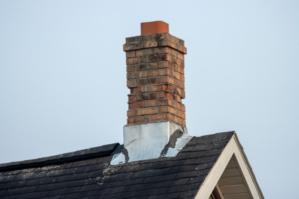 An old brick chimney on a shingled roof